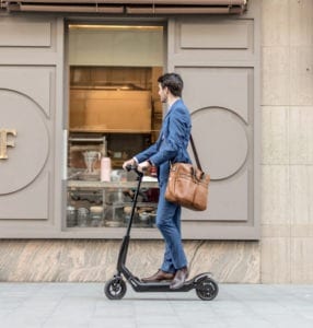 A young business man riding an electric scooter downtown