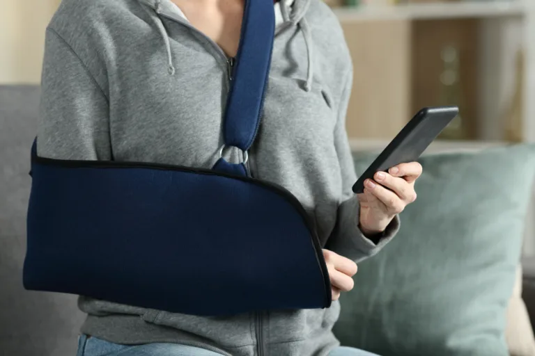 Woman with broken arm wearing sling using smart phone