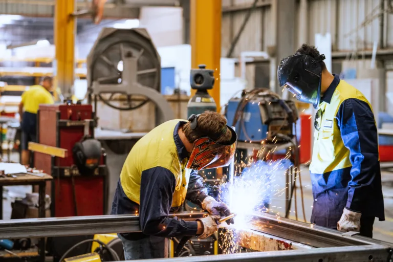 Worker in protective gear welding metal in an industrial factory setting with sparks flying around brightly illuminating the area