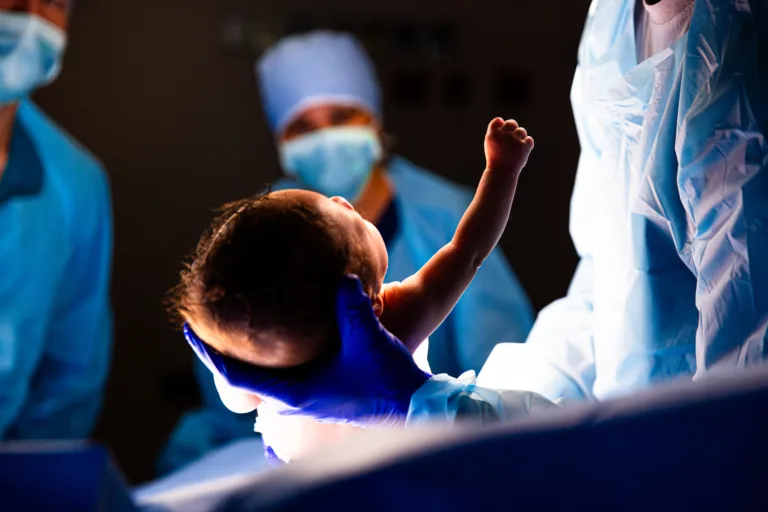 Baby delivered and raising arm and fist during C Section procedure in Hospital Operating Room